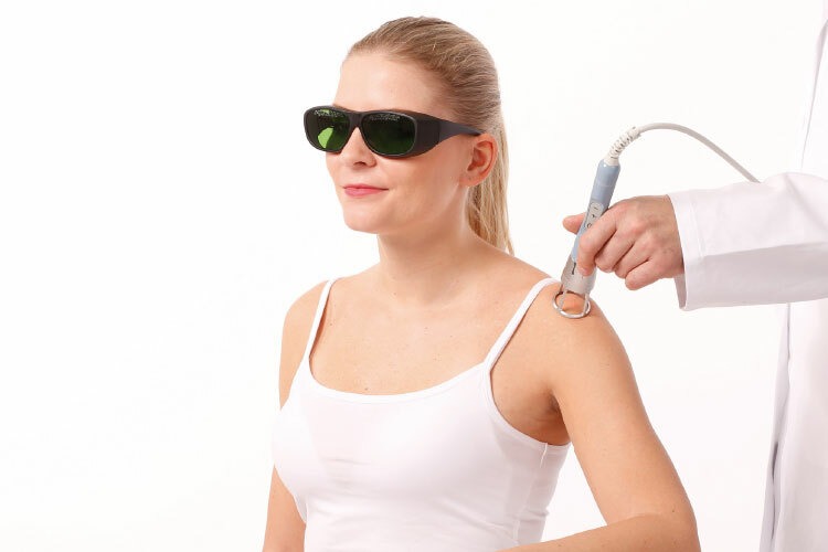 Žena v ochranných brýlích podstupuje laserovou terapii na kůži prováděnou odborníkem, zdůrazňující bezpečnost a profesionální péči.